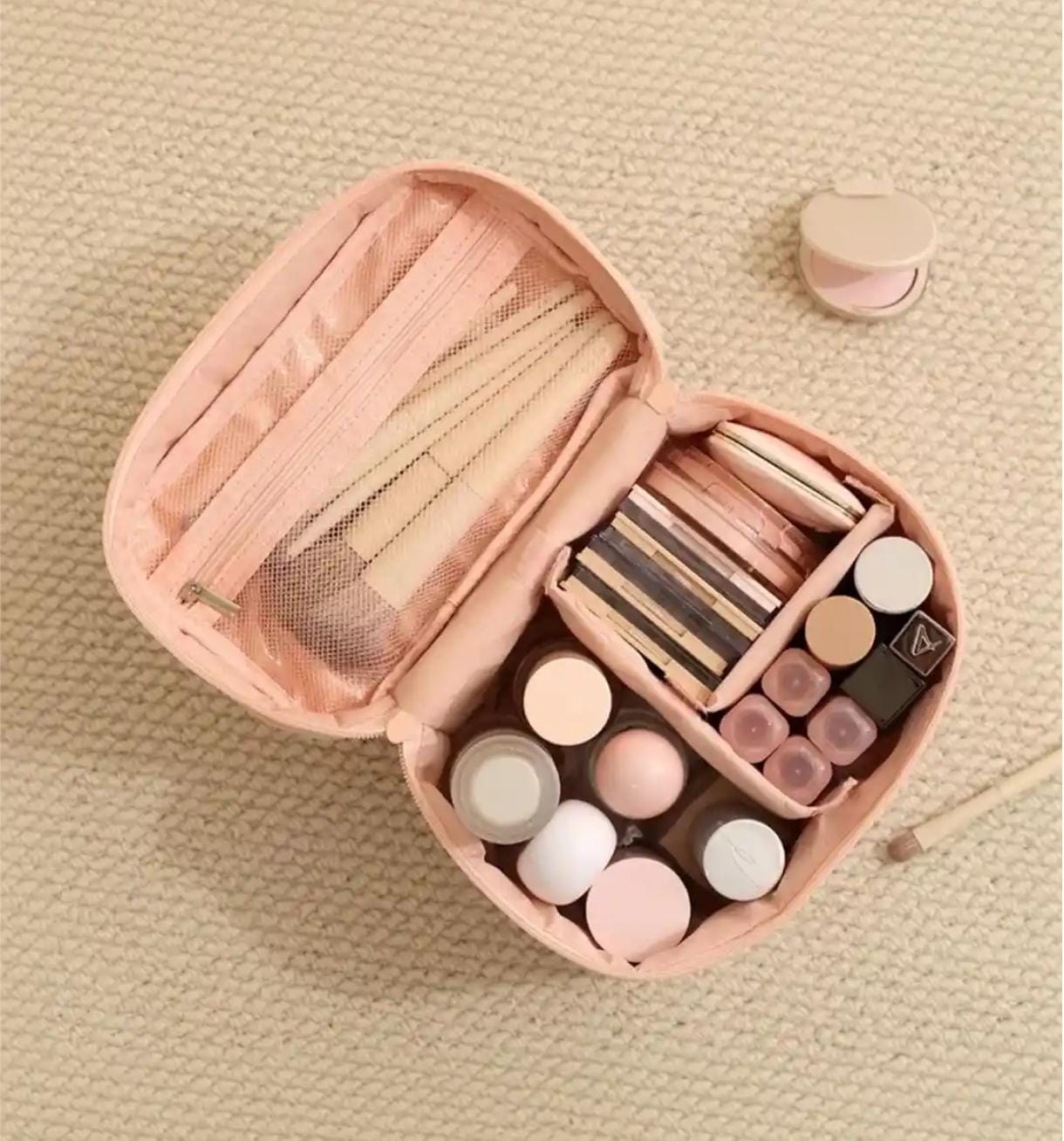 Open pink makeup case with various cosmetic items on a beige textured background