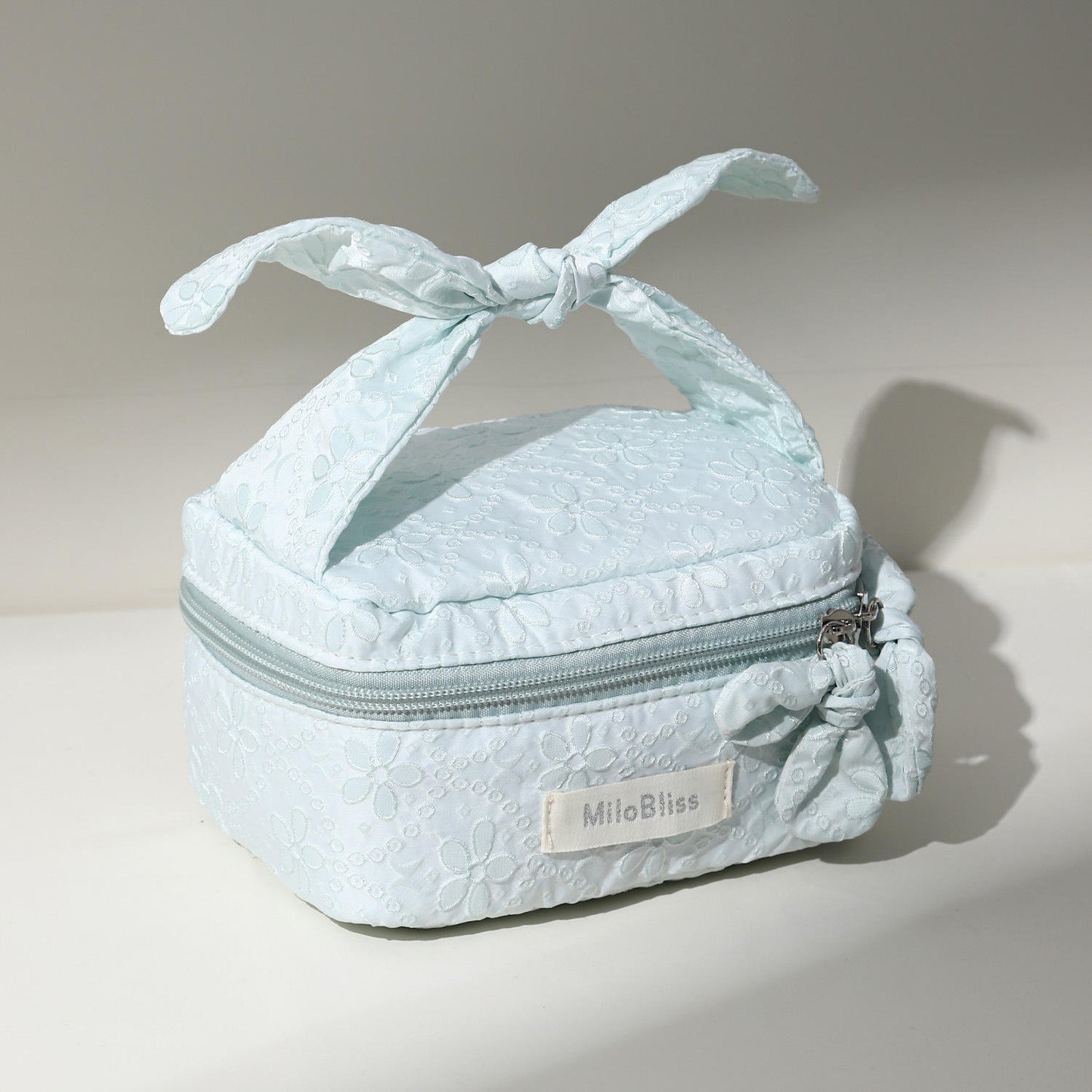 Light blue textured makeup bag with a bow on top, featuring the brand 'MilaBliss'.