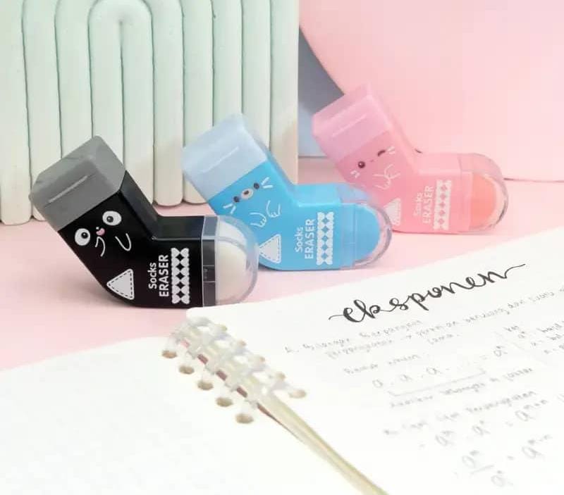Three colorful erasers on a surface with a piece of paper and a pen.