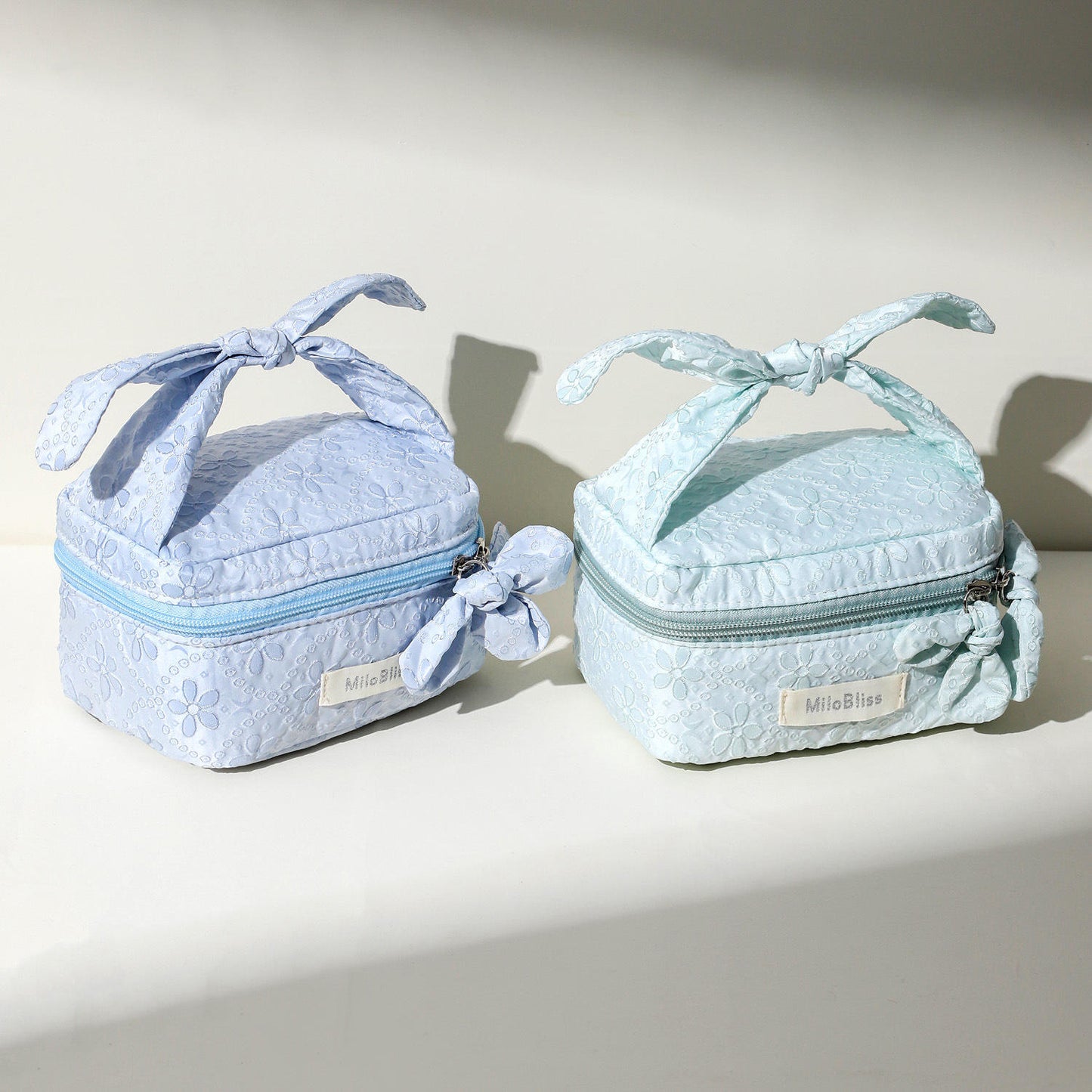 Two light blue cosmetic bags with ribbons on a neutral background