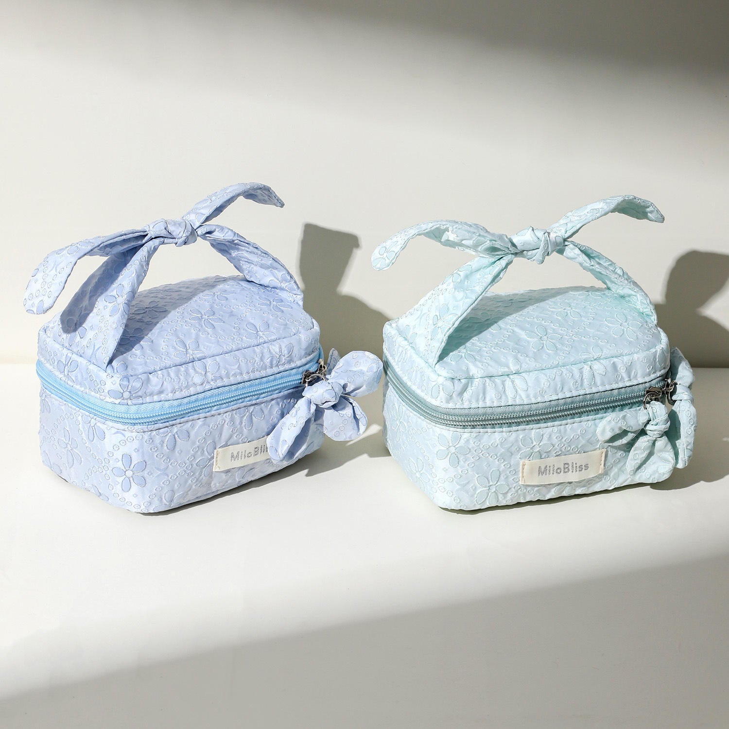 Two light blue cosmetic bags with ribbons on a neutral background