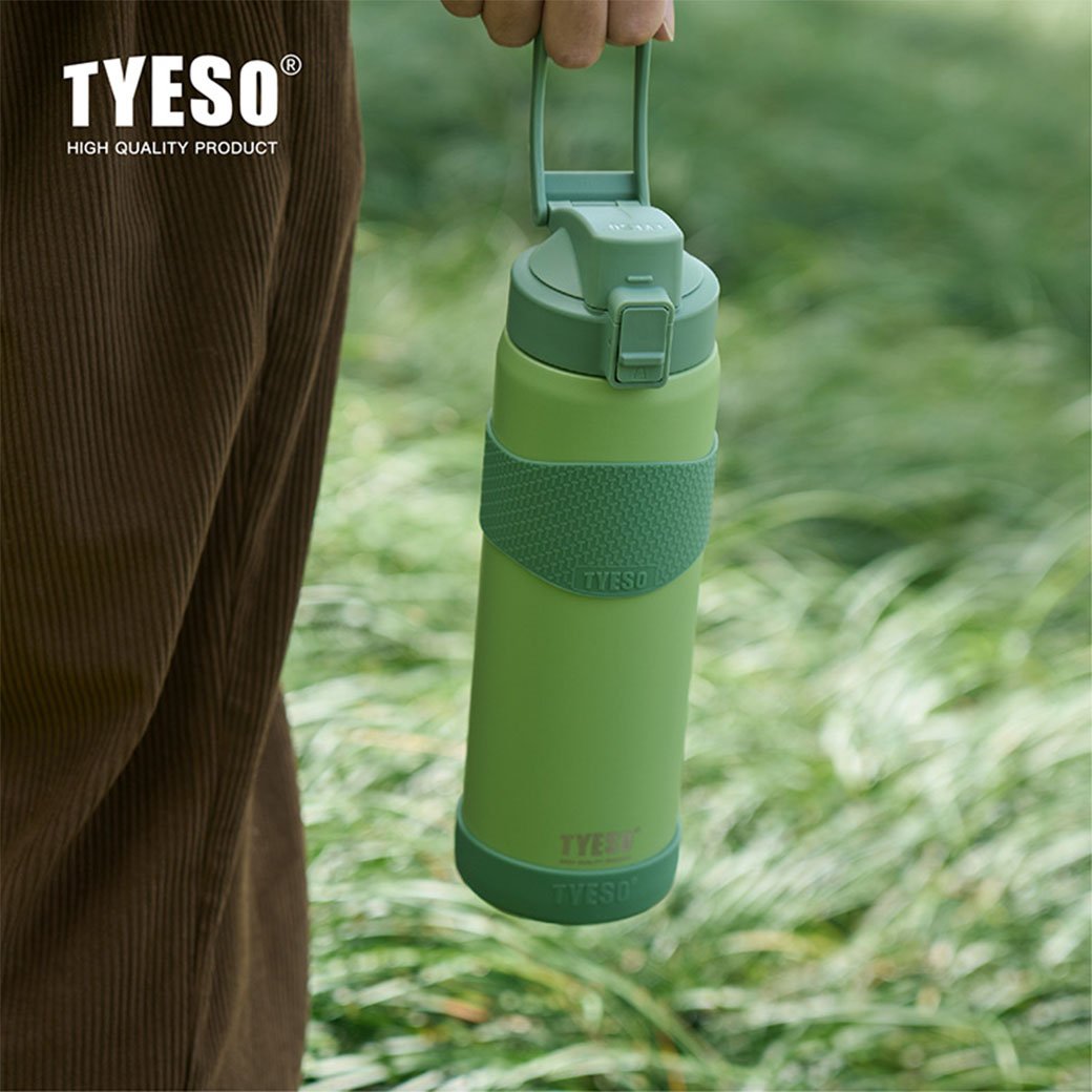 Green water bottle held by a person in a grassy outdoor setting with TYESO branding.