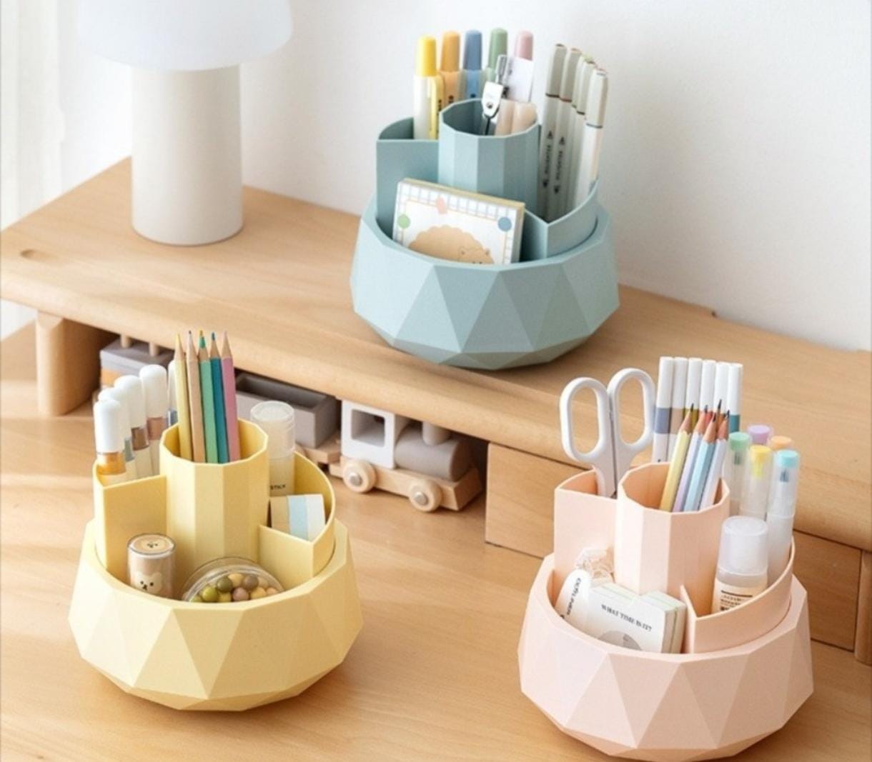 Set of geometric desk organizers in yellow, blue, and pink with stationery items on a wooden surface.
