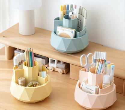 Set of geometric desk organizers in yellow, blue, and pink with stationery items on a wooden surface.