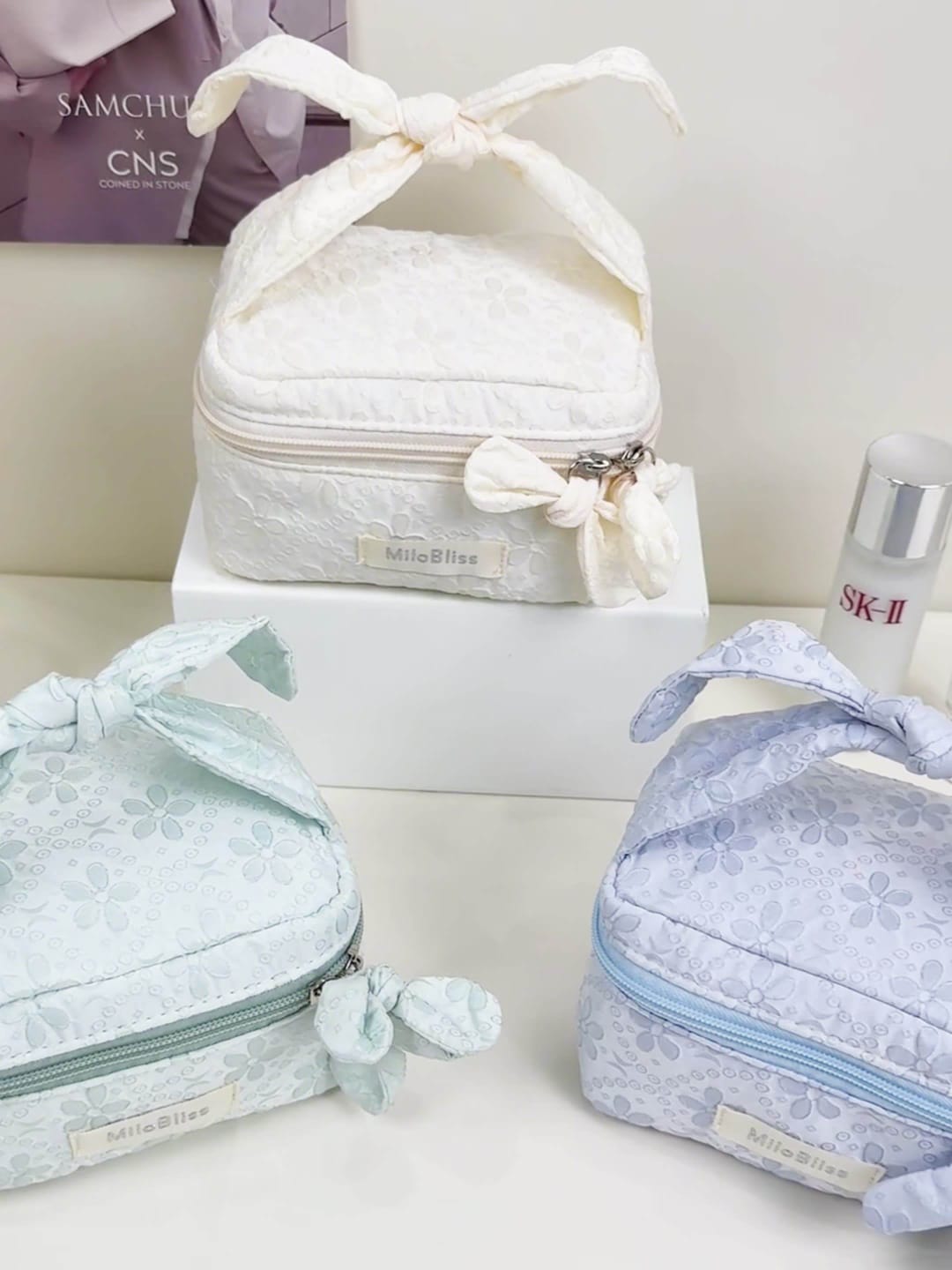 Set of three lace-trimmed cosmetic bags with a bottle of SK-II on a white surface.