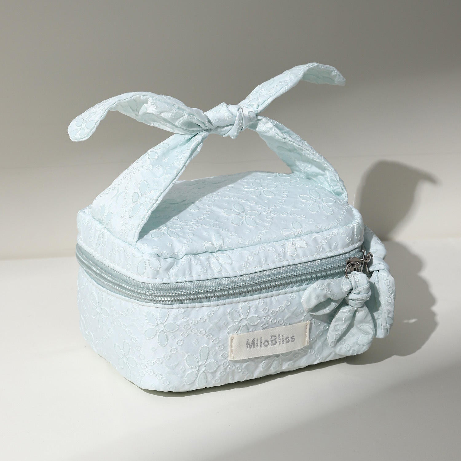 Light blue textured makeup bag with a bow on top, featuring the brand 'MilaBliss'.