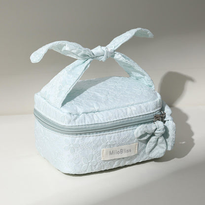 Light blue textured makeup bag with a bow on top, featuring the brand 'MilaBliss'.